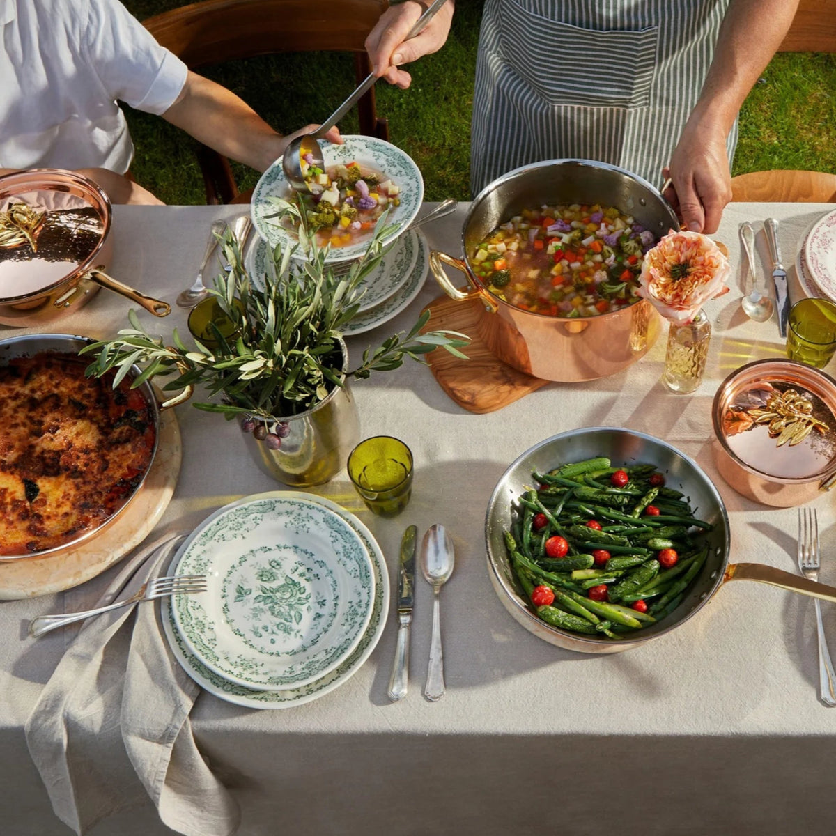 Olivia Cupra collection on a beige linen tablecloth with green plates and glasses in the Italian countryside on a summer day