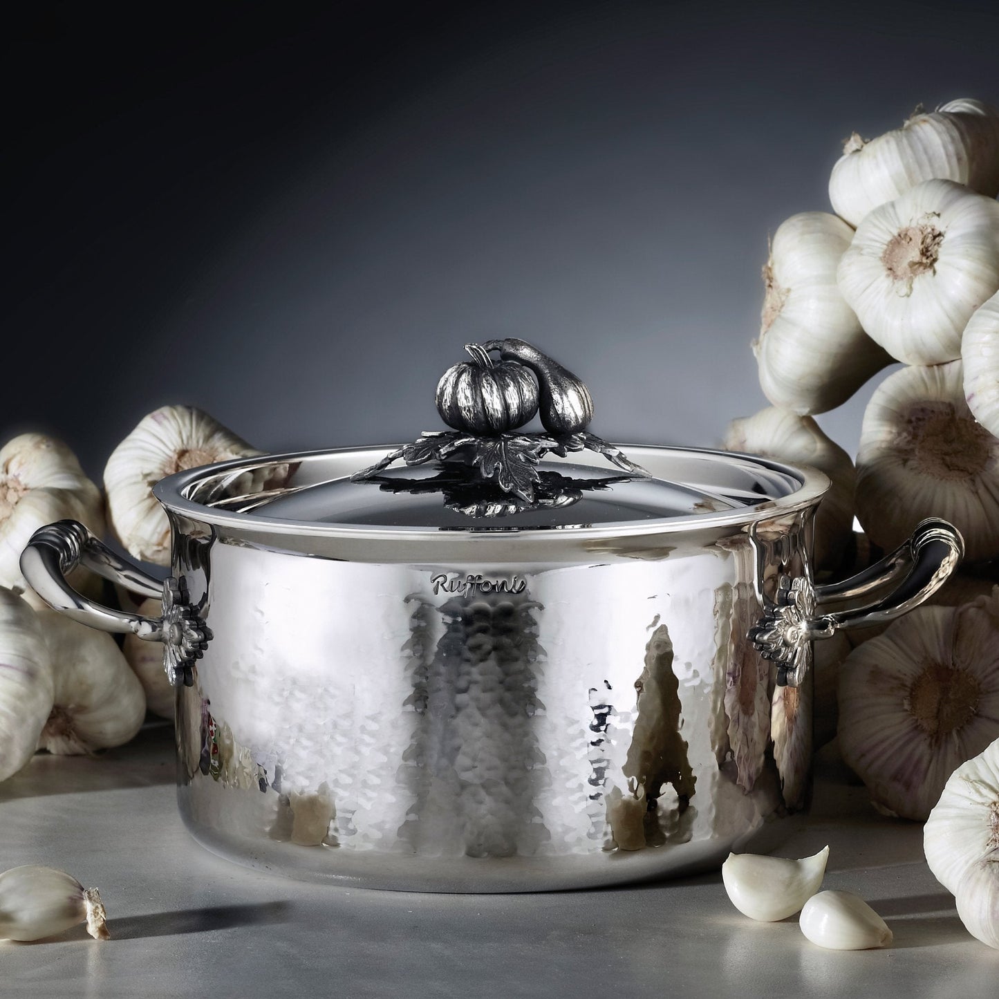 Opus Prima hammered clad stainless steel soup pot with decorated silver-plated lid knob finial from Ruffoni on a garlic background
