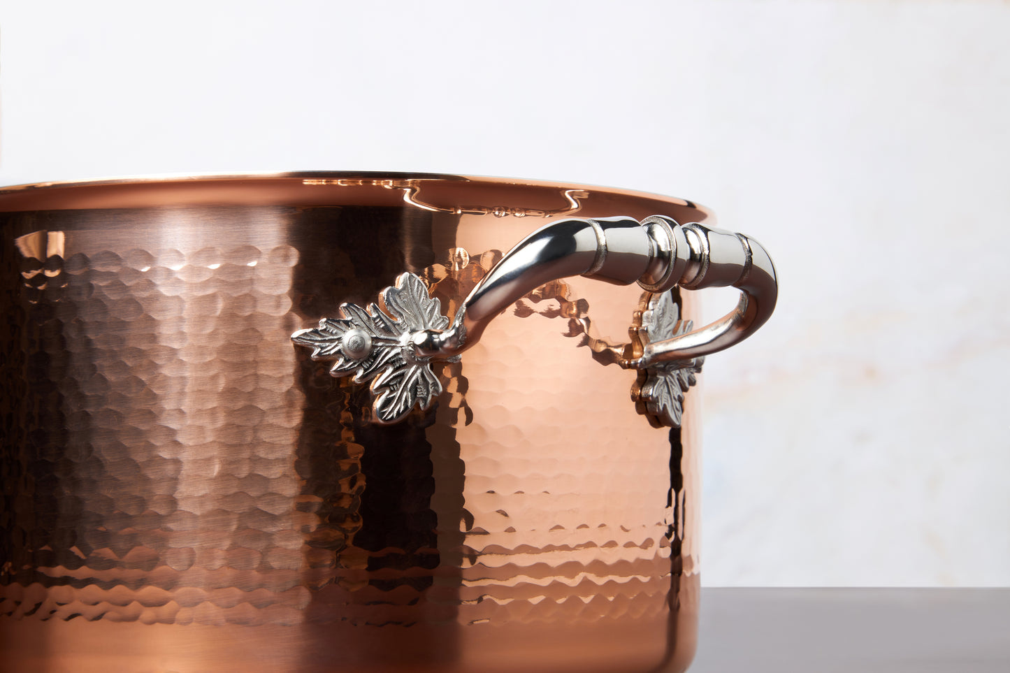 Beautiful stainless steel helper handle decorated with delicate leaves on Opus Cupra cookware by Ruffoni