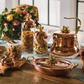 lotus 5 piece set including a copper tea kettle, copper 10" roaster and a set of 3 kitchen glass jars in glass and copper, all topped by lotus-shaped bronze knobs