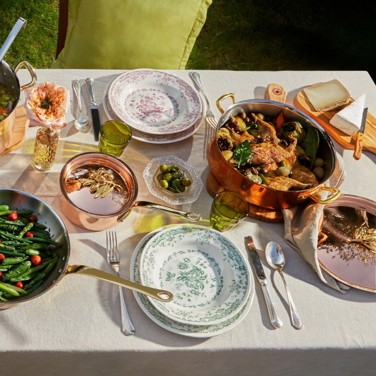 Olivia Cupra 6 piece set on a beige linen tablecloth with green plates and glasses in the Italian countryside on a summer day