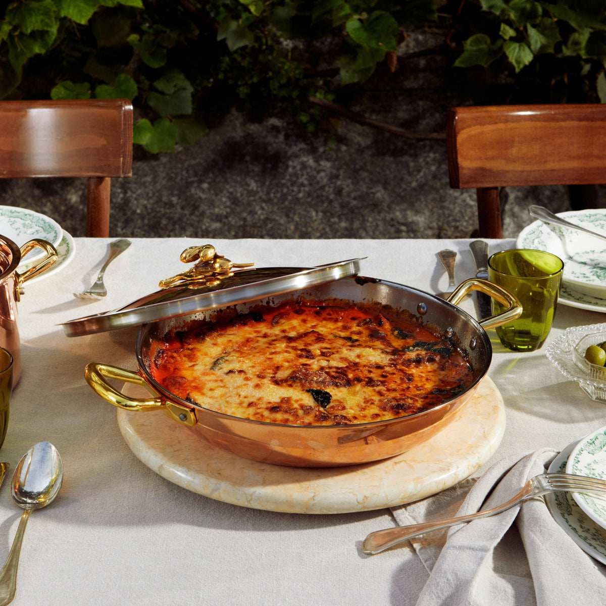 Olivia Cupra Serving Frying Pan on a beige linen tablecloth with green plates and glasses in the Italian countryside on a summer day