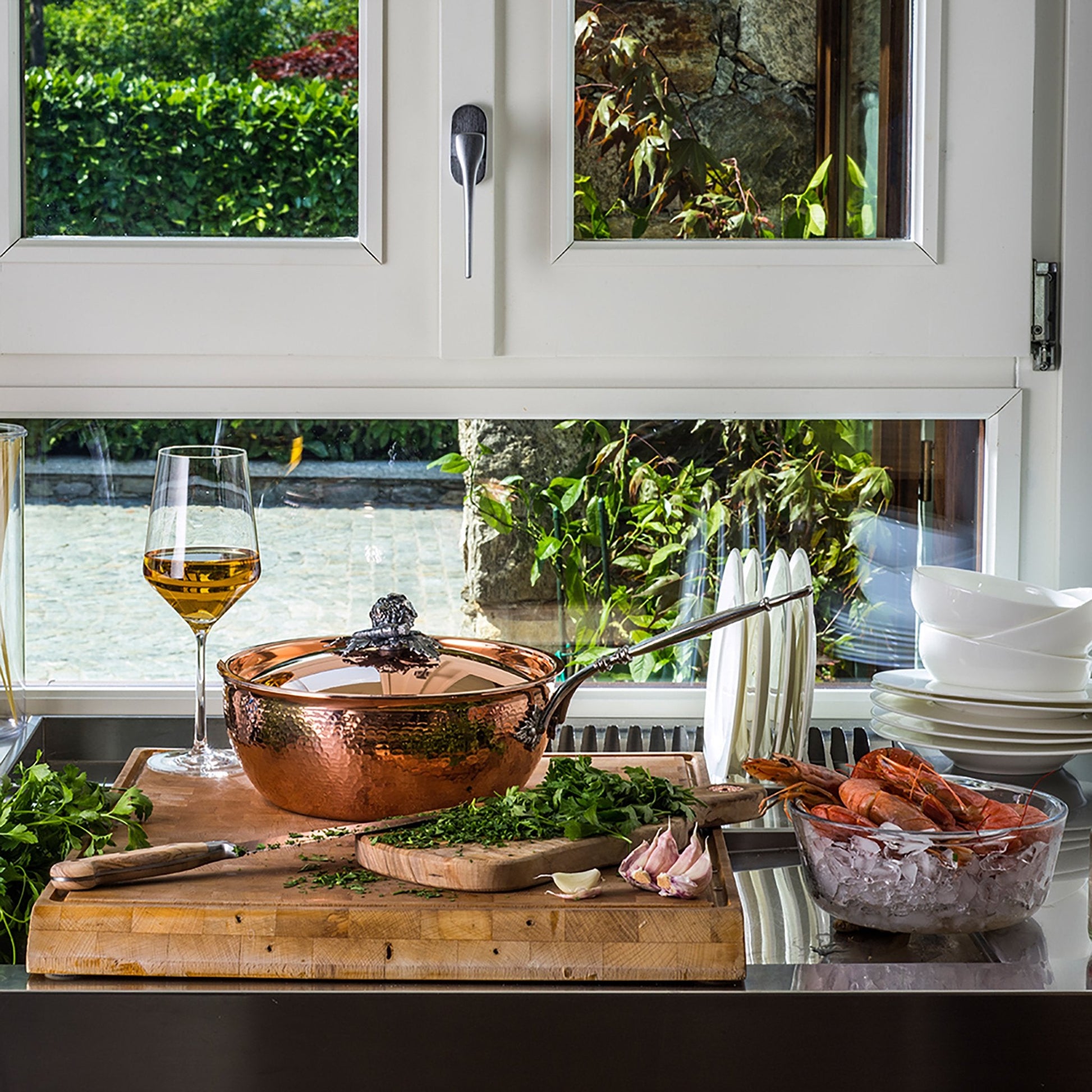 Hand-hammered, copper chef pan with stainless steel lining in the kitchen with chopped herbs and shellfish